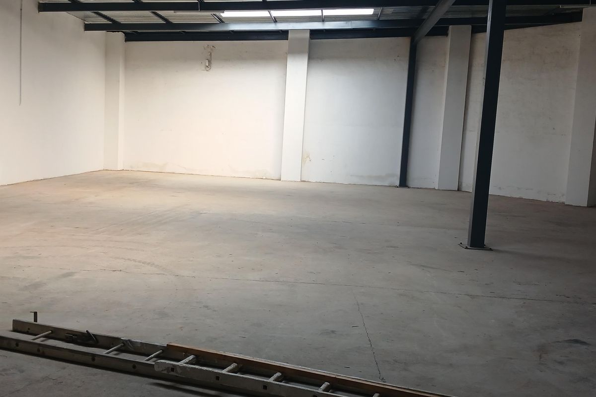 Spacious industrial utility area featuring exposed steel structural beams, concrete flooring, and natural light from a ceiling skylight.