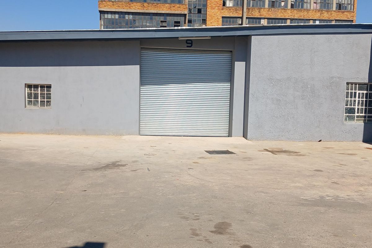 Industrial unit exterior featuring a large roller shutter door, security-barred windows, and a paved concrete apron area.