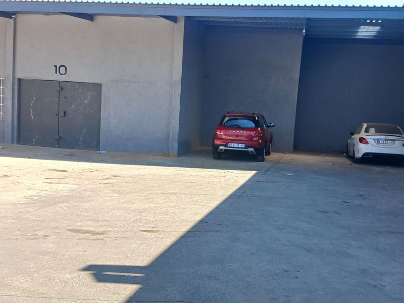 Industrial exterior view featuring a concrete hardstand, covered loading area, and secure steel access door with window security bars.
