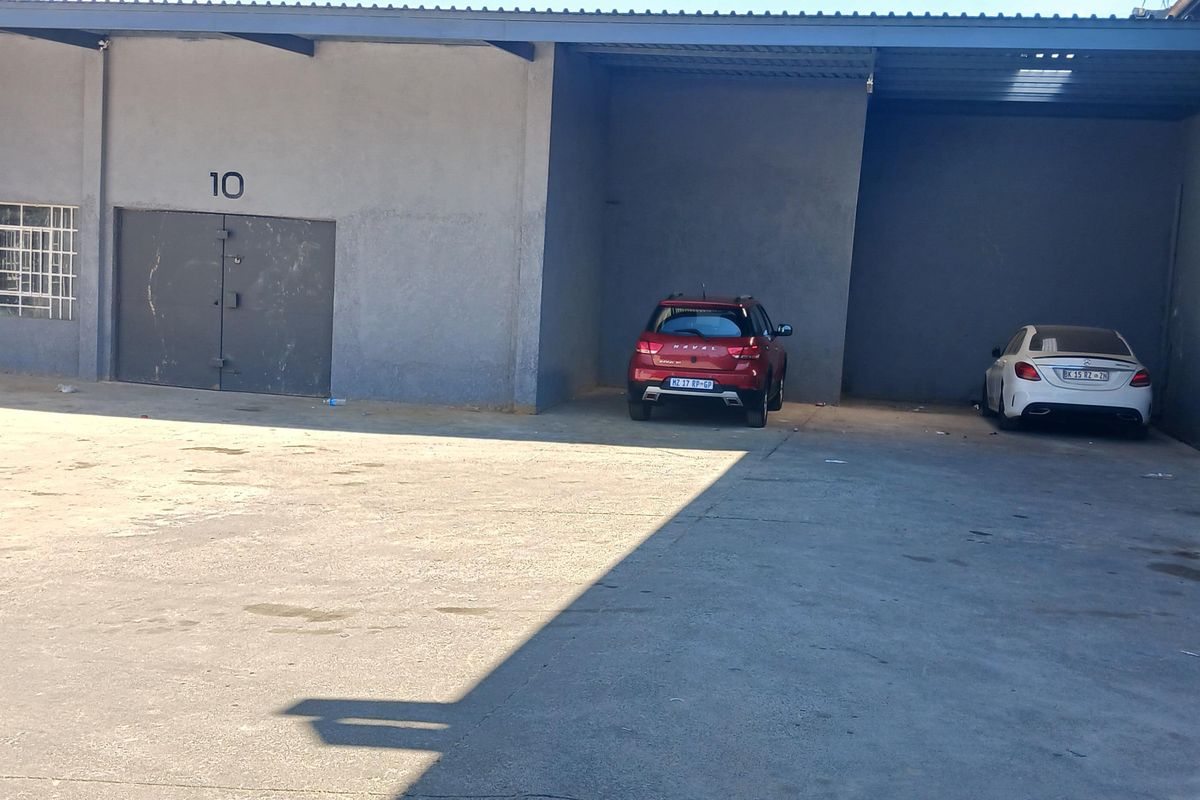 Industrial exterior view featuring a concrete hardstand, covered loading area, and secure steel access door with window security bars.