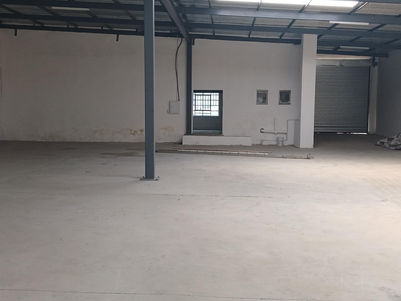 Spacious industrial warehouse unit featuring high ceilings, concrete flooring, and a large roller shutter door for easy access.