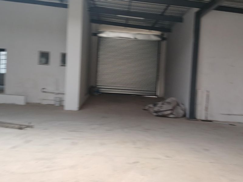 Spacious industrial utility area featuring high ceilings with exposed steel beams, concrete flooring, and a large roller shutter door for easy access.