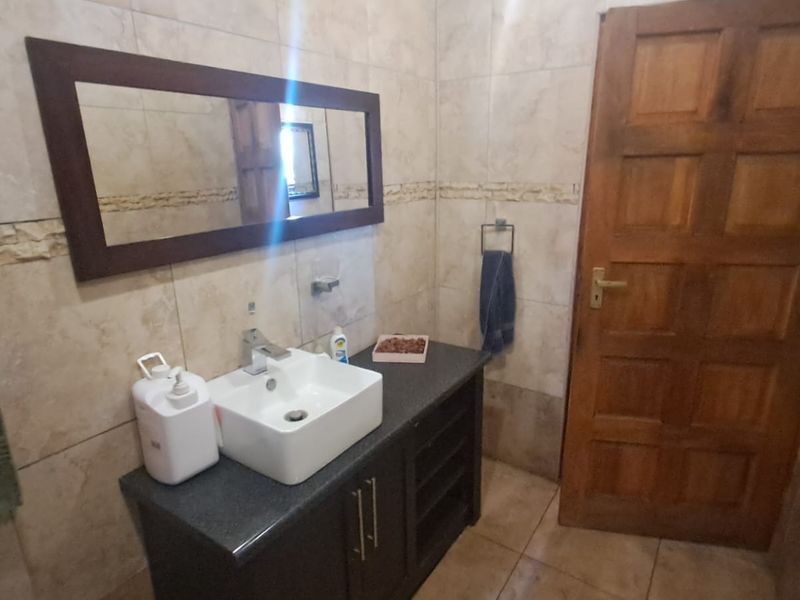A functional bathroom featuring a modern vessel sink on a dark vanity cabinet, complemented by neutral wall tiling and a solid timber door.