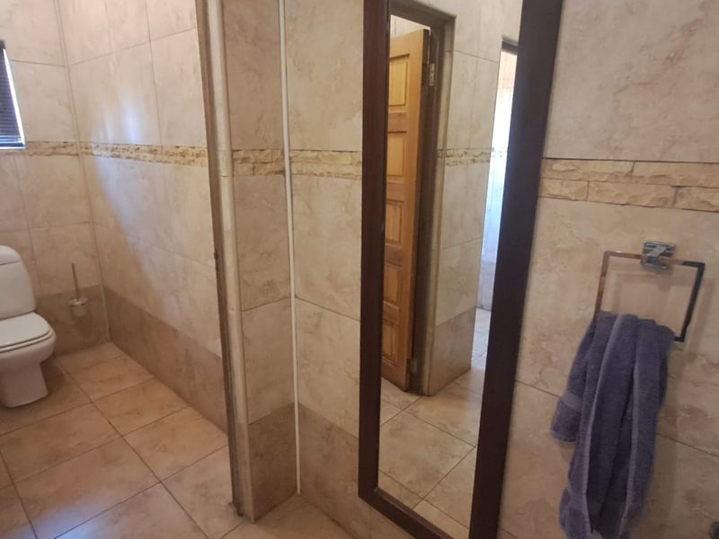 A functional bathroom featuring full-height wall tiling, floor tiles, a standard toilet, and a window with blinds.