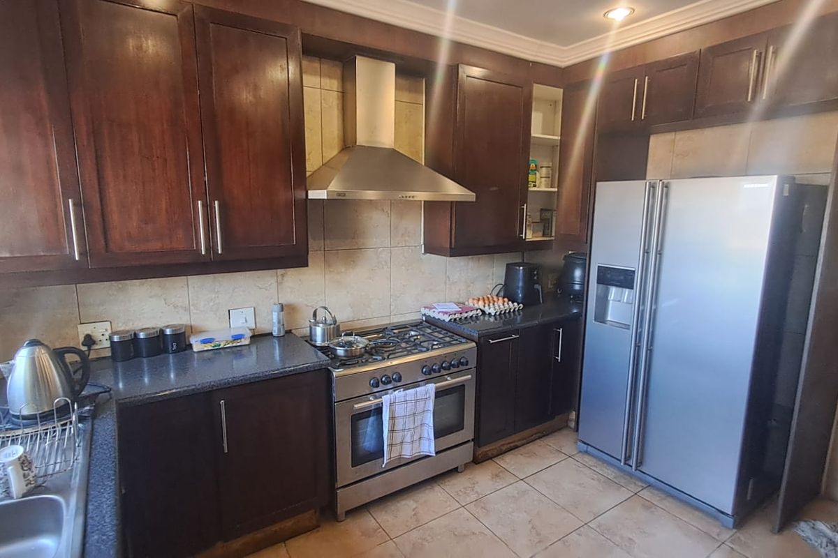 A functional kitchen featuring dark wood cabinetry, a stainless steel gas stove with extractor fan, tiled backsplash, and tiled flooring.