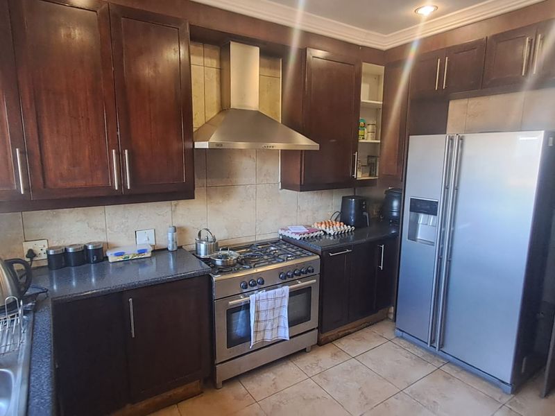 A functional kitchen featuring dark wood cabinetry, a stainless steel gas stove with extractor fan, tiled backsplash, and tiled flooring.