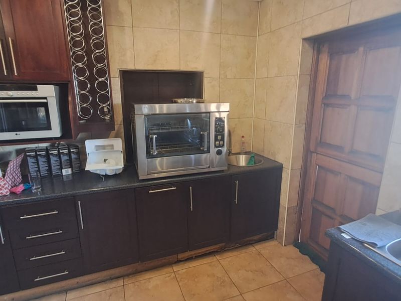 A functional scullery area featuring dark wood cabinetry, granite countertops, built-in oven and microwave, and tiled finishes throughout.