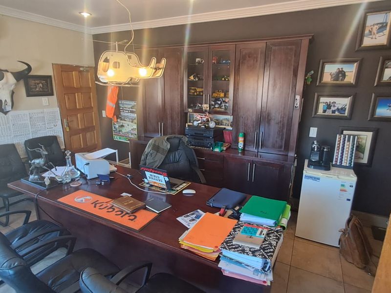 A functional office space featuring extensive built-in wooden cabinetry, tiled flooring, and a wall-mounted air conditioning unit.