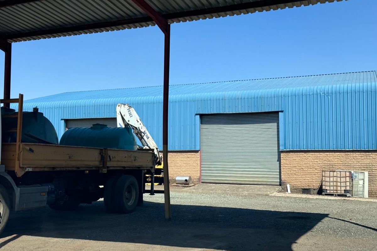Industrial warehouse exterior featuring a blue corrugated metal roof, brick facade, and a large roller shutter door with a covered loading bay.