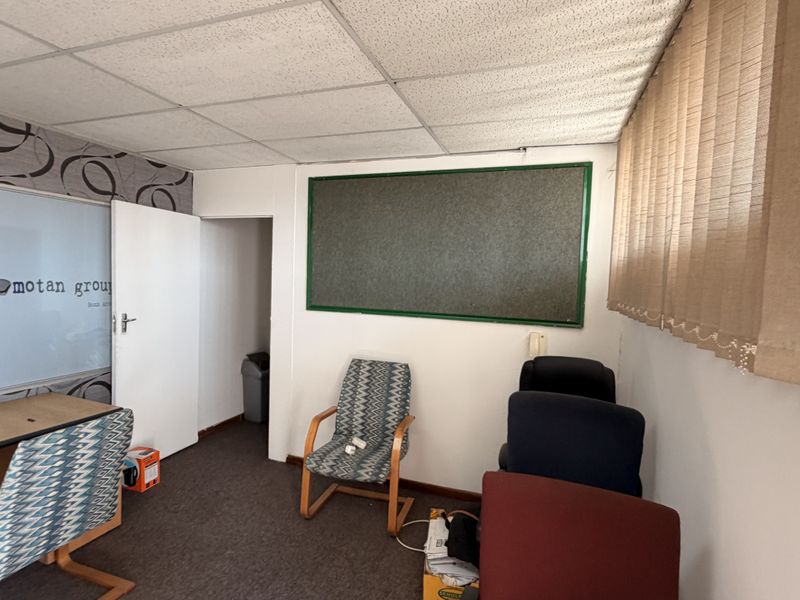 A functional office space featuring a suspended ceiling, vertical window blinds, and carpeted flooring, suitable for a professional work environment.