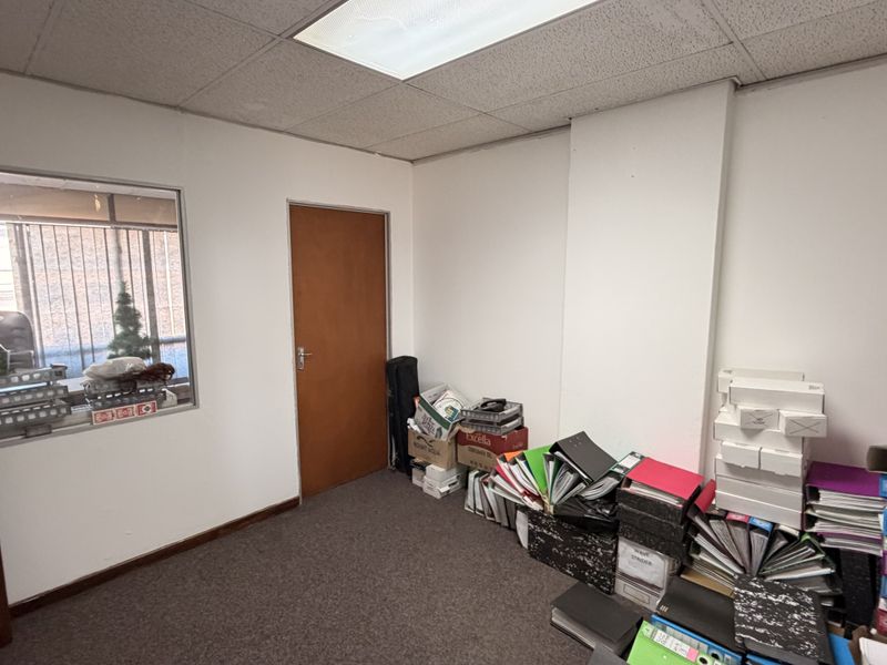 A functional office space featuring carpeted flooring, a suspended ceiling with recessed lighting, and an internal window providing natural light.