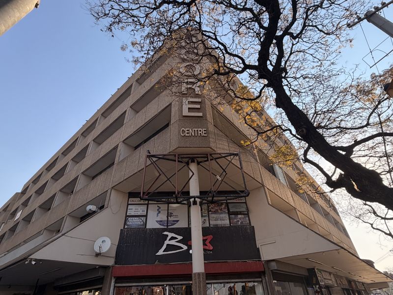 A low-angle view of a multi-story commercial office building facade featuring street-level retail units and prominent signage.
