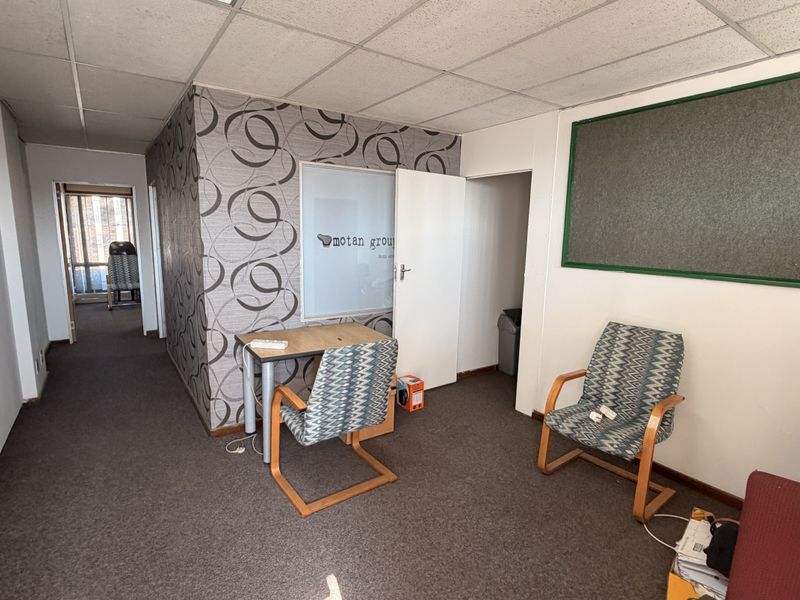 A functional office space featuring a suspended ceiling, carpeted flooring, and a built-in notice board, suitable for a professional work environment.