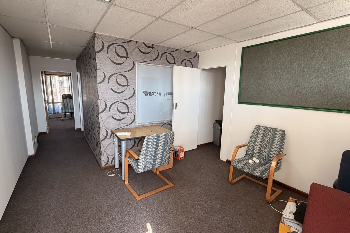 A functional office space featuring a suspended ceiling, carpeted flooring, and a built-in notice board, suitable for a professional work environment.