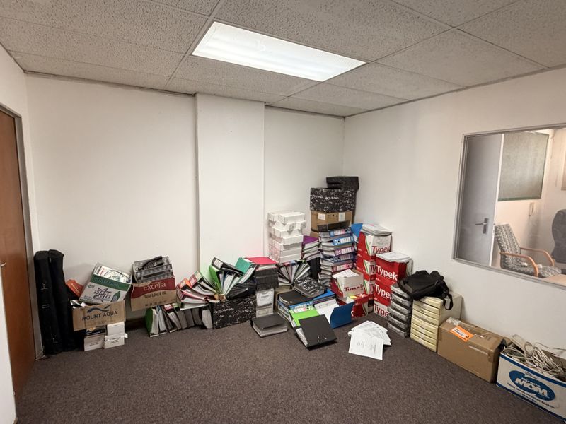 A functional office space featuring a drop ceiling, recessed lighting, and an internal glass partition, currently utilized for storage.