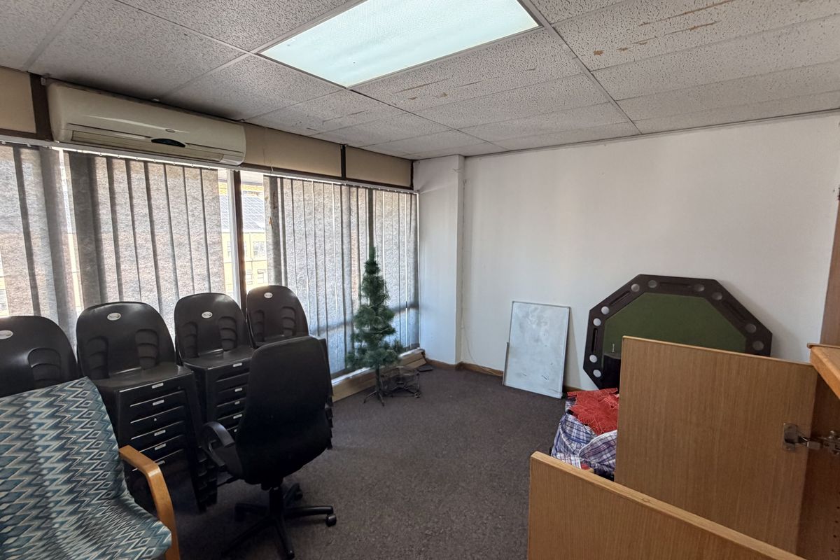A functional office space featuring a drop ceiling with recessed lighting, wall-mounted air conditioning, and large windows with vertical blinds.