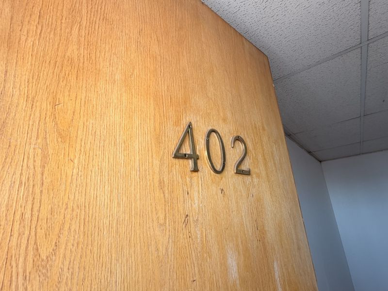 A close-up view of a wooden office door marked with the number 402, featuring a standard drop ceiling above.