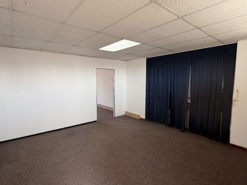 An empty office space featuring a suspended ceiling with recessed lighting, carpeted flooring, and dark vertical blinds covering the window area.