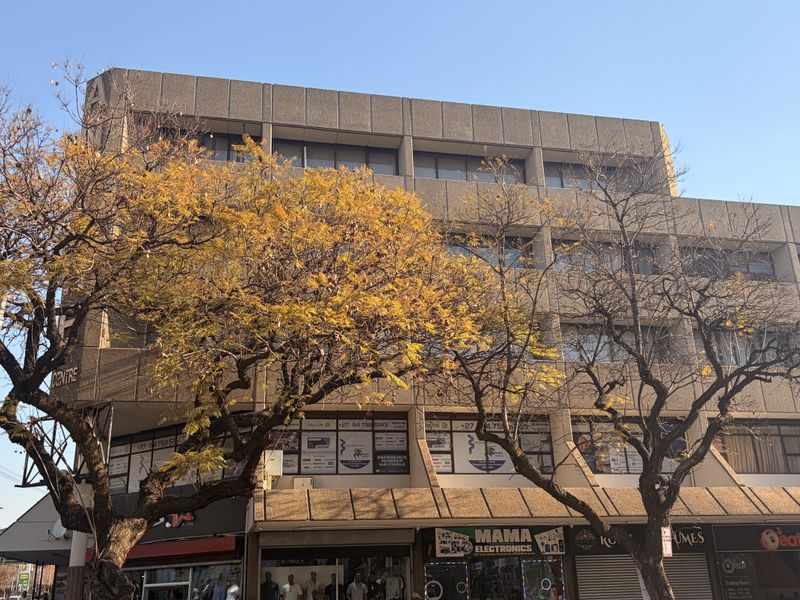 A multi-story commercial office building featuring a concrete facade with ground-level retail storefronts and large windows.
