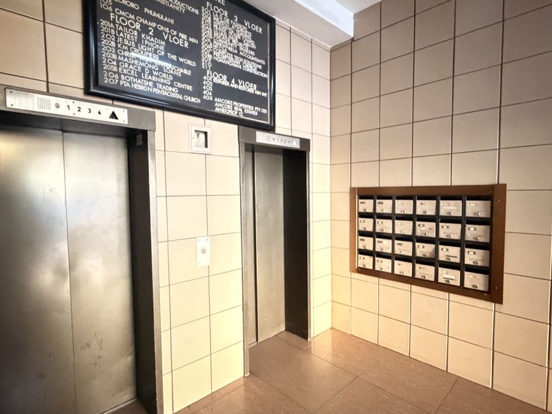 Office building lobby entrance featuring stainless steel elevators, a tenant directory board, and a bank of built-in mailboxes with tiled wall finishes.
