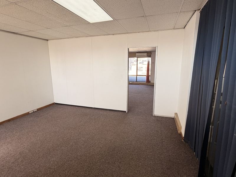 An empty office space featuring a suspended ceiling, recessed lighting, and carpet flooring, with a doorway leading to an adjacent room.