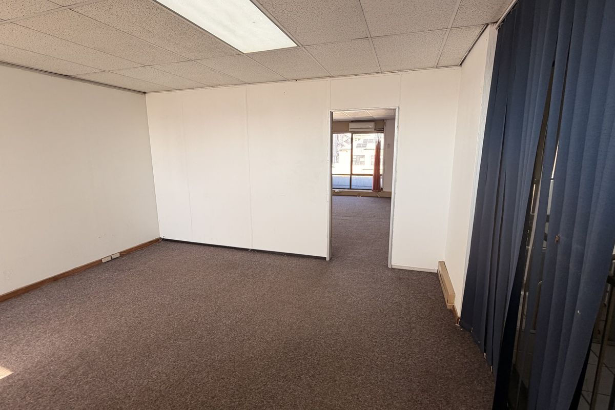 An empty office space featuring a suspended ceiling, recessed lighting, and carpet flooring, with a doorway leading to an adjacent room.