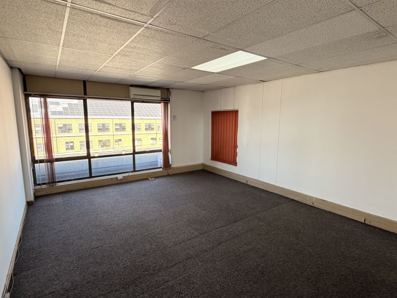 An empty office space featuring a suspended ceiling, recessed lighting, air conditioning, and large windows with vertical blinds.
