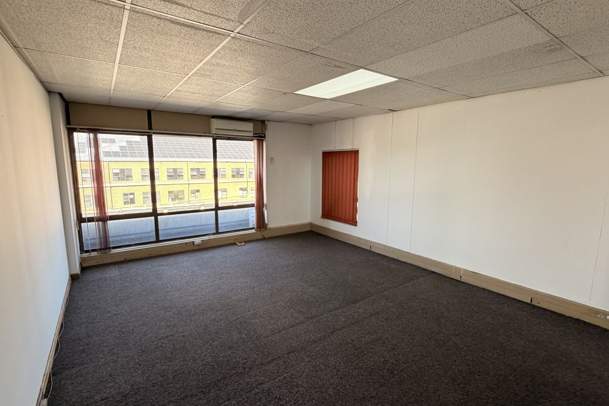 An empty office space featuring a suspended ceiling, recessed lighting, air conditioning, and large windows with vertical blinds.