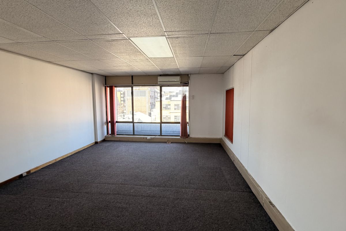 An empty, open-plan office space featuring a suspended ceiling, recessed lighting, split-system air conditioning, and large windows providing natural light.