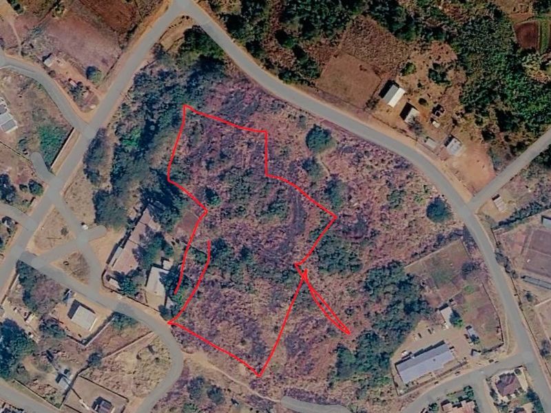 Aerial view of a vacant commercial land plot with road access, outlined in red for boundary identification.