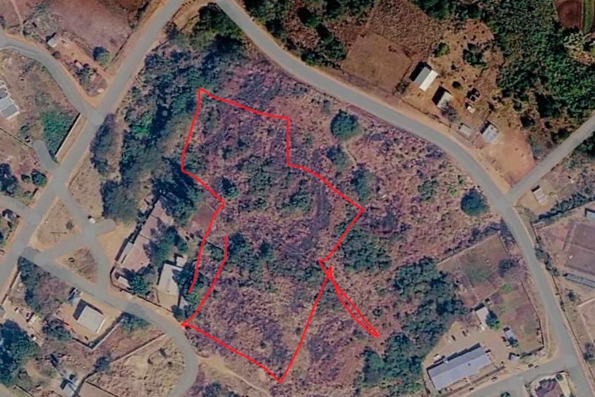 Aerial view of a vacant commercial land plot with road access, outlined in red for boundary identification.