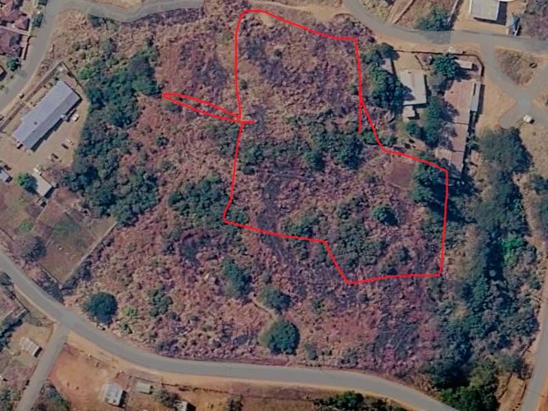 Aerial view of a vacant commercial land plot with natural vegetation and defined boundary lines.