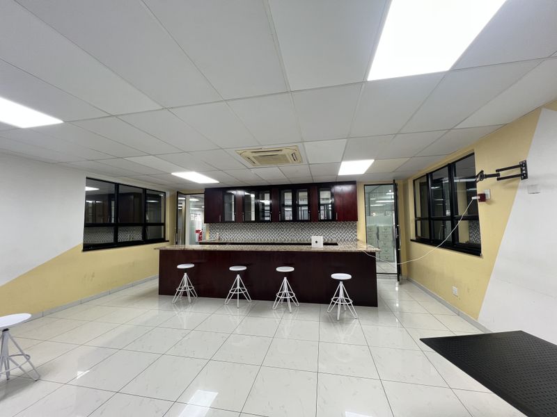 A modern office breakroom featuring dark wood cabinetry, a granite-topped breakfast bar, tiled flooring, and recessed ceiling lighting.