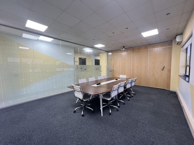 A professional office boardroom featuring a glass partition wall, timber paneling, suspended ceiling with recessed lighting, and carpeted flooring.