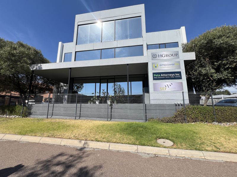Modern multi-level office building featuring a prominent glass facade, professional business signage, and secure perimeter fencing.