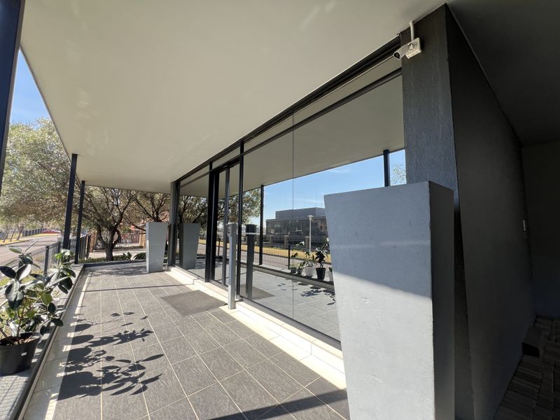 A modern, covered outdoor patio area featuring large glass office frontage, tiled flooring, and integrated security infrastructure.