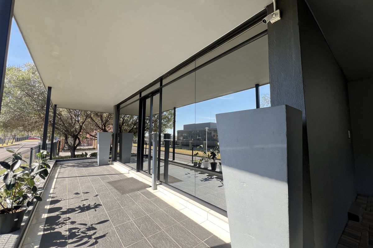 A modern, covered outdoor patio area featuring large glass office frontage, tiled flooring, and integrated security infrastructure.