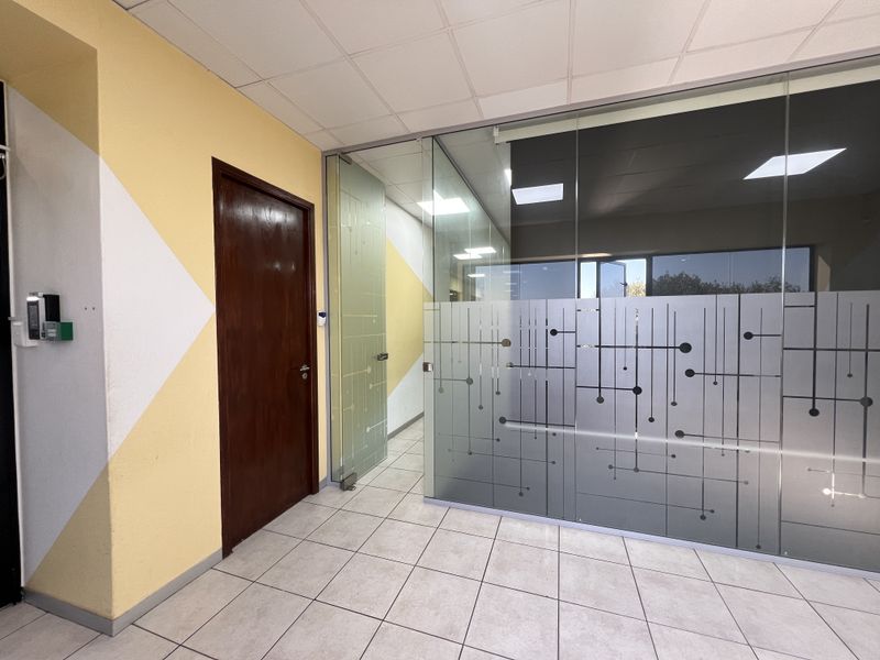 A bright office space featuring a modern glass partition wall, suspended ceiling with recessed lighting, and clean ceramic floor tiles.