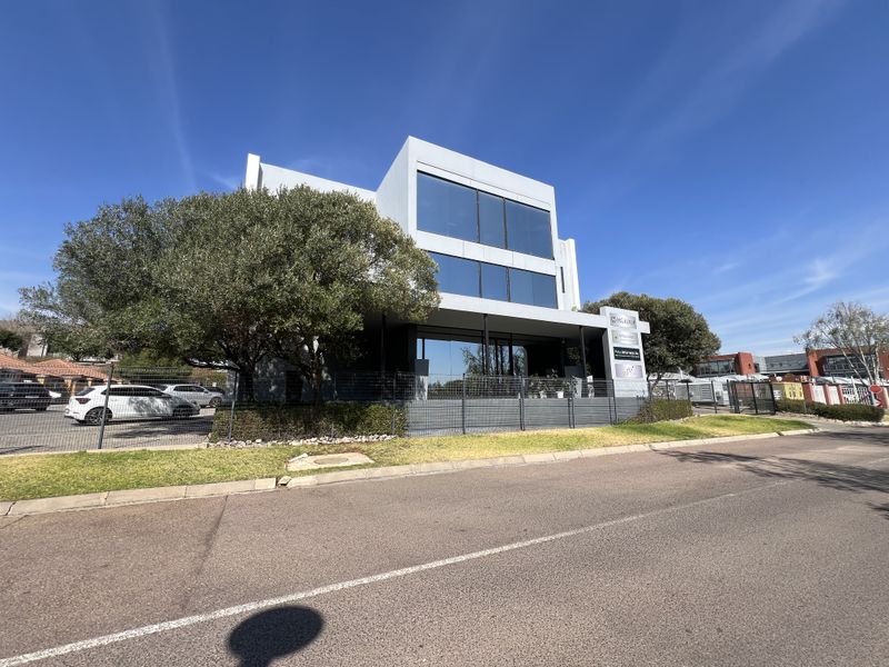 Modern multi-story office building featuring large glass windows, a covered entrance, and well-maintained perimeter fencing and landscaping.