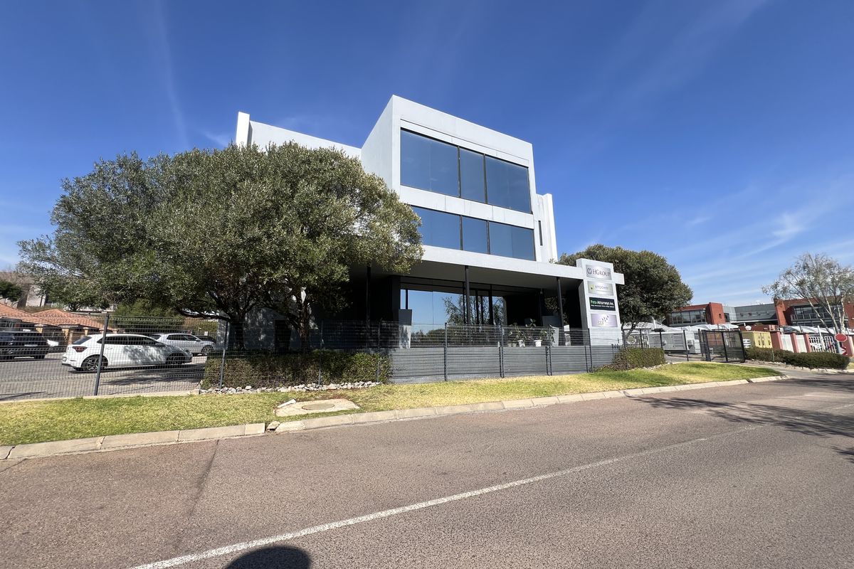 Modern multi-story office building featuring large glass windows, a covered entrance, and well-maintained perimeter fencing and landscaping.