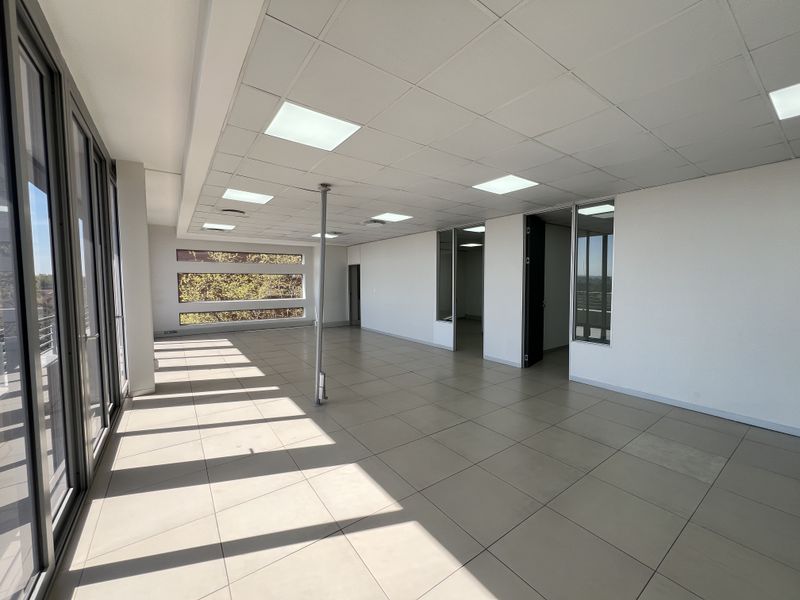 A bright, open-plan office space featuring ceramic tiled flooring, suspended ceilings with recessed lighting, and modern aluminium-framed glass partitions.