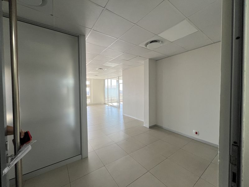 A bright, vacant office space featuring a suspended ceiling, tiled flooring, and glass partitions, offering a clean and professional environment.