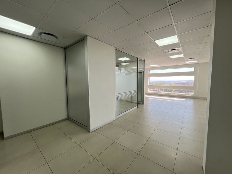 A bright, open-plan office space featuring modern glass partitions, suspended ceilings with recessed lighting, and large windows offering natural light and scenic views.