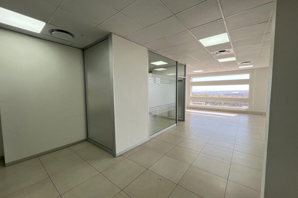 A bright, open-plan office space featuring modern glass partitions, suspended ceilings with recessed lighting, and large windows offering natural light and scenic views.