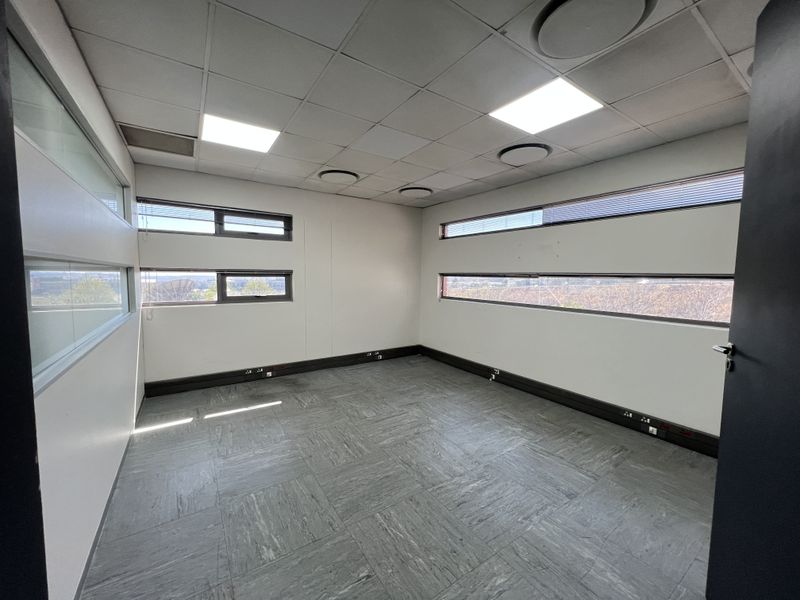 A clean, empty office space featuring modern vinyl flooring, suspended ceiling with recessed lighting, and horizontal windows providing natural light.
