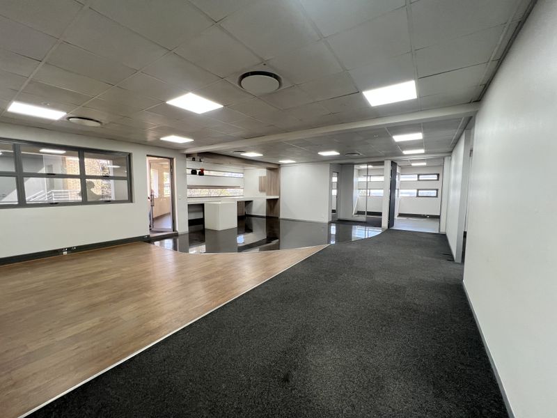 Spacious open-plan office area featuring a modern suspended ceiling, recessed lighting, and a combination of wood-look and carpeted flooring with built-in reception counter.