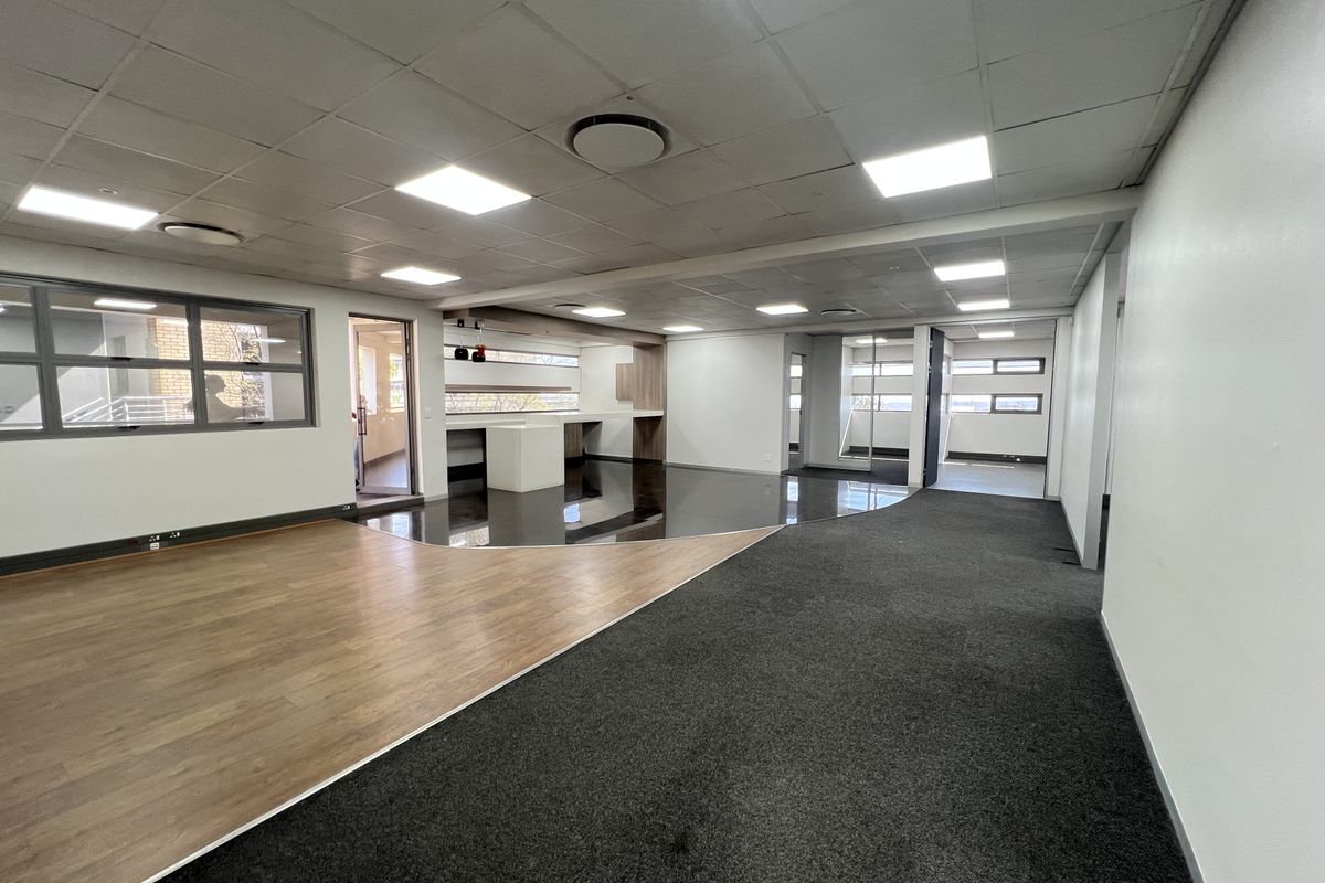 Spacious open-plan office area featuring a modern suspended ceiling, recessed lighting, and a combination of wood-look and carpeted flooring with built-in reception counter.