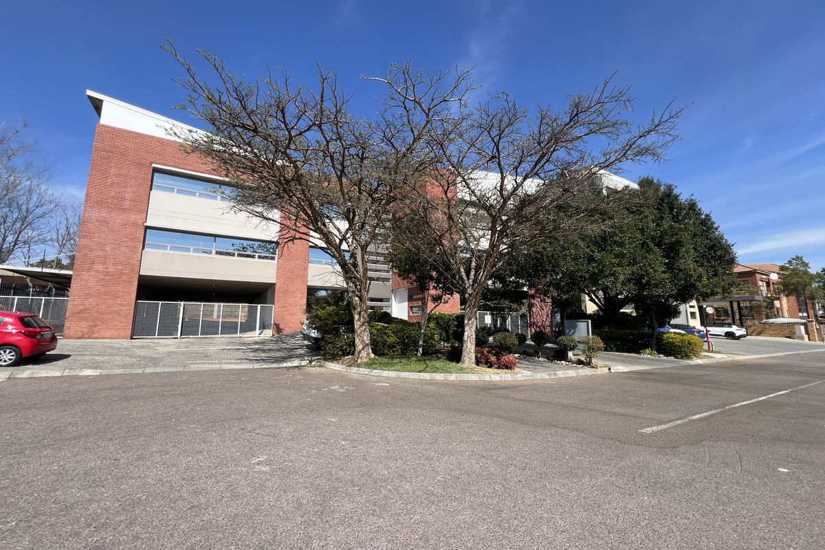 Front exterior view of a multi-story office building featuring a red brick facade, paved parking area, and established landscaping.