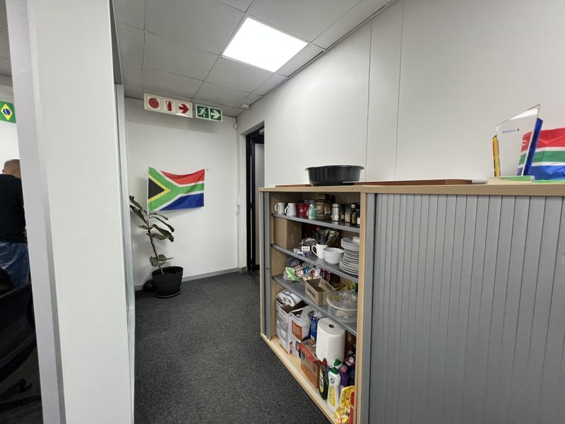A functional office hallway featuring recessed ceiling lighting, emergency exit signage, and carpeted flooring, providing access to adjacent office spaces.