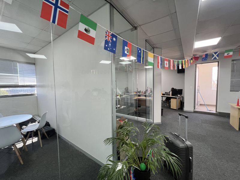 Modern office space featuring glass partition walls, carpeted flooring, and a suspended ceiling with recessed lighting, providing a professional and open work environment.